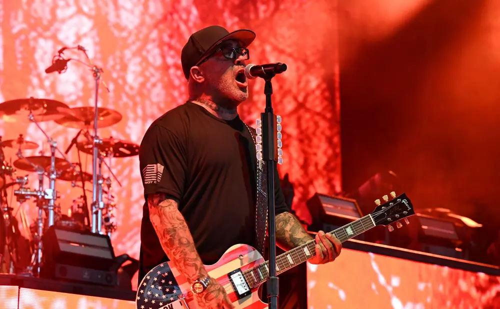 A man in a black t-shirt and baseball cap sings and plays a guitar painted like the American flag.