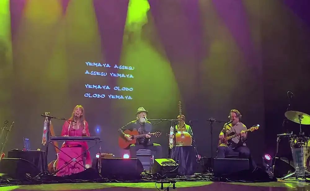 A band performs on stage with lyrics projected behind them.