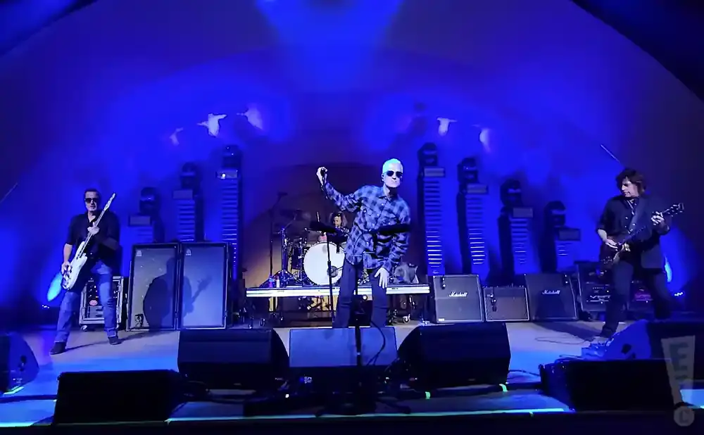 Three musicians perform on a stage illuminated by blue lights.