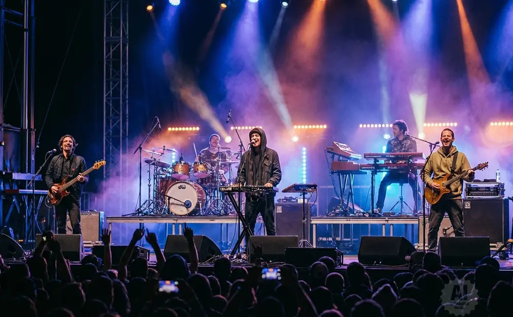 A band performs on stage with colorful lights and smoke, with a guitarist in the foreground and a crowd watching.