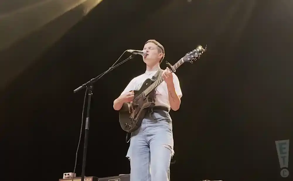 A person plays a guitar and sings into a microphone on a dark stage.