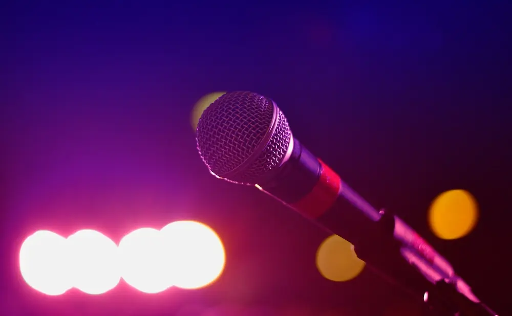 A microphone on a stand against a blurred backdrop of purple and pink lights.