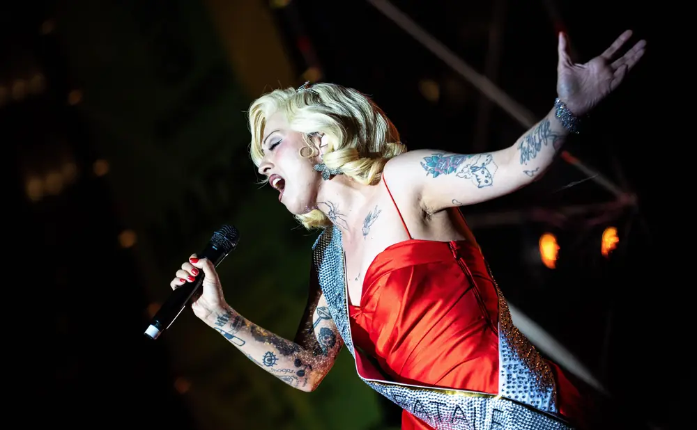 A tattooed woman in a red dress sings into a microphone on stage.