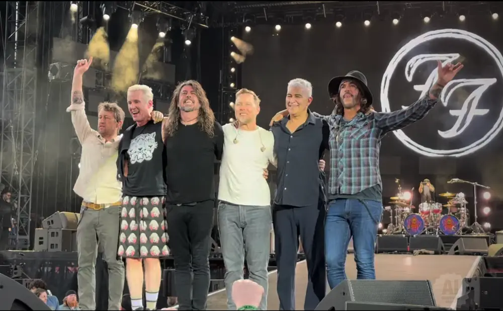Foo Fighters band members pose on stage with arms around each other.