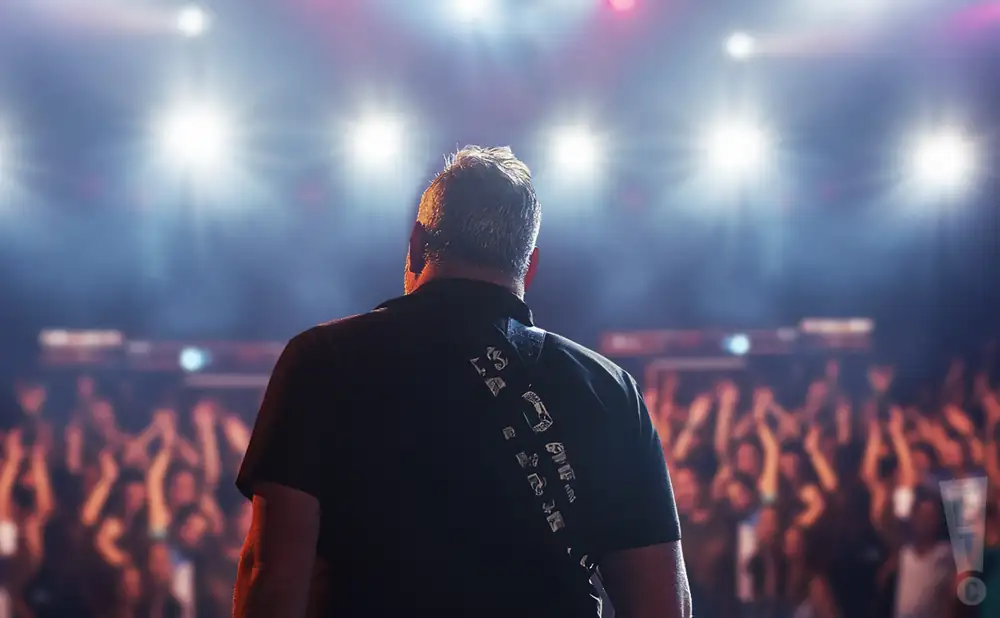 a rear view photo of greg dulli performing a concert on stage to a lively audience