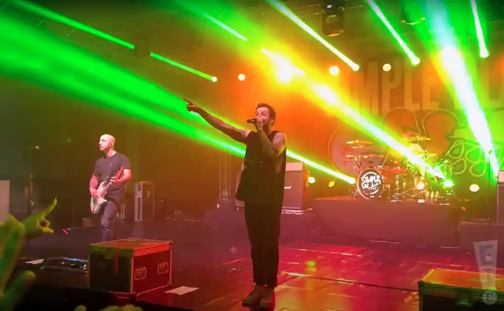 simple plan singer on stage with green lights beaming behind him
