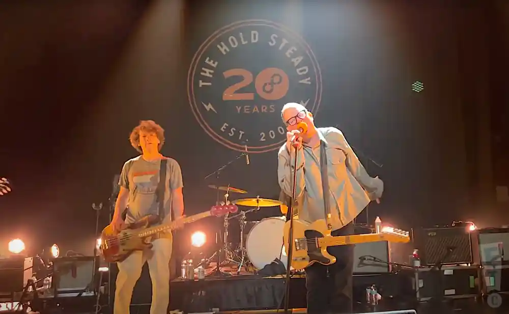 the hold steady electric guitarist and bassist performing in orange light