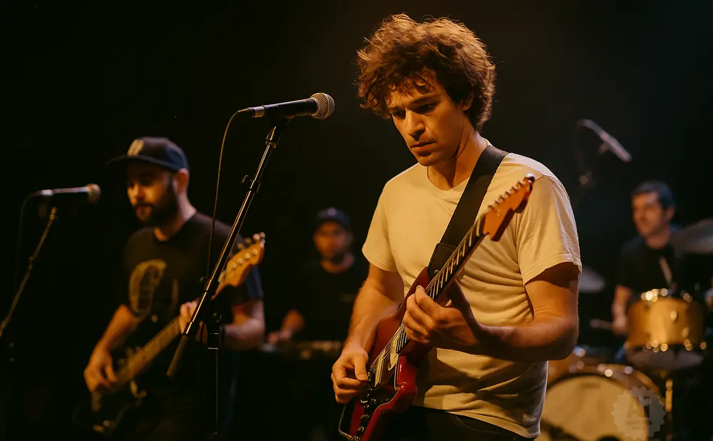 A band performs on stage, with a guitarist in the foreground playing a red guitar.