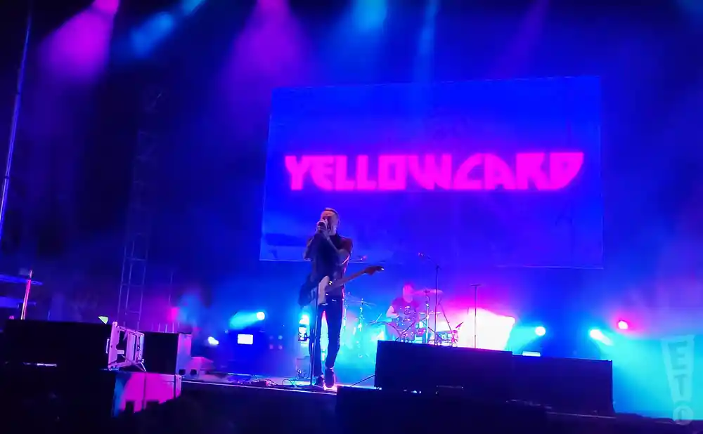 yellowcard playing live on stage with their name on screen behind them