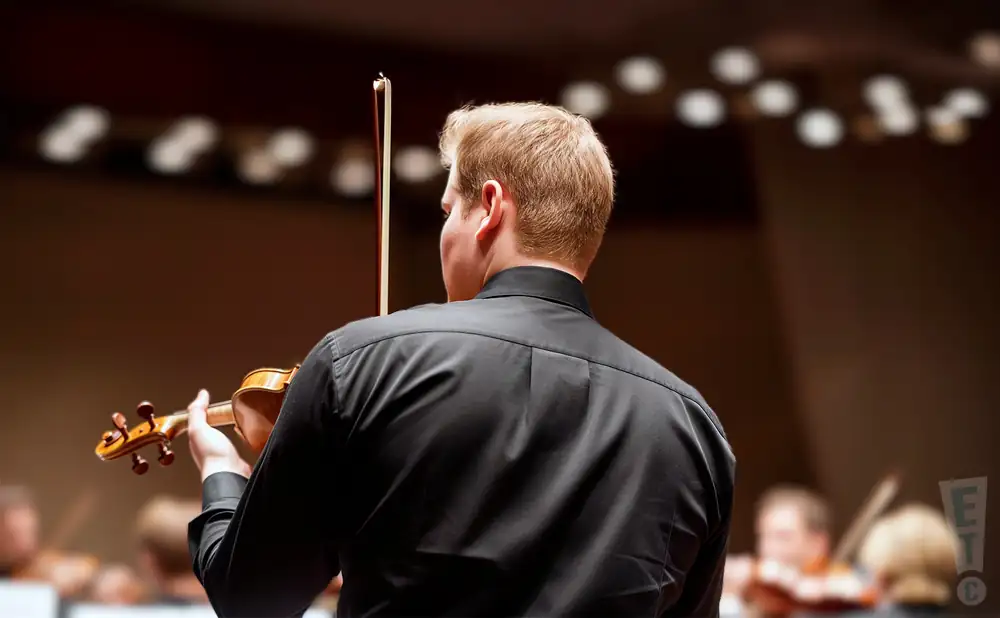 a rear view photo of jonathan crow performing a concert on stage to a lively audience