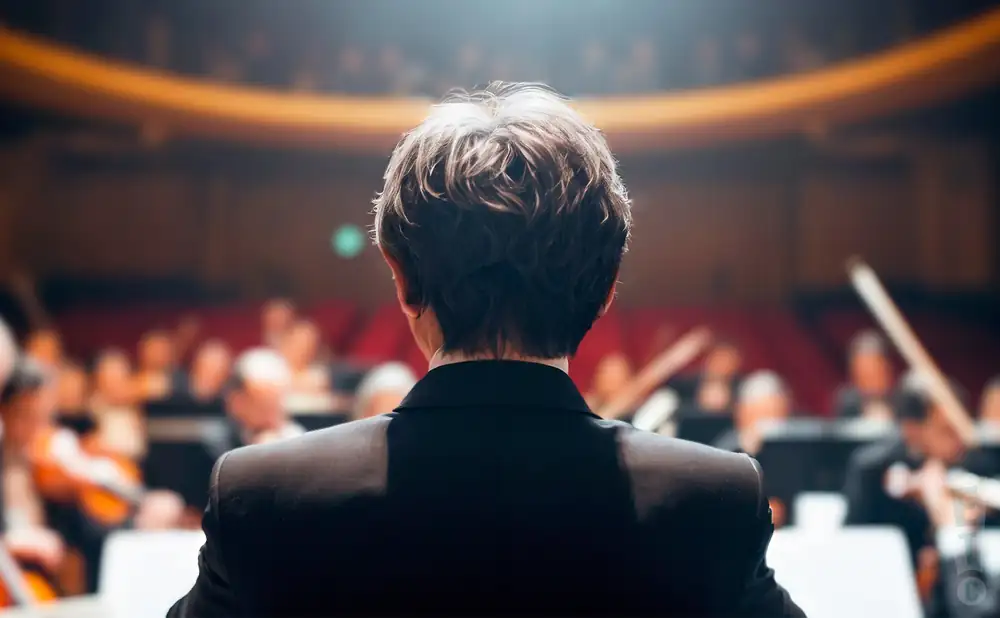 a rear view photo of jun markl conducting a symphony on stage before an audience
