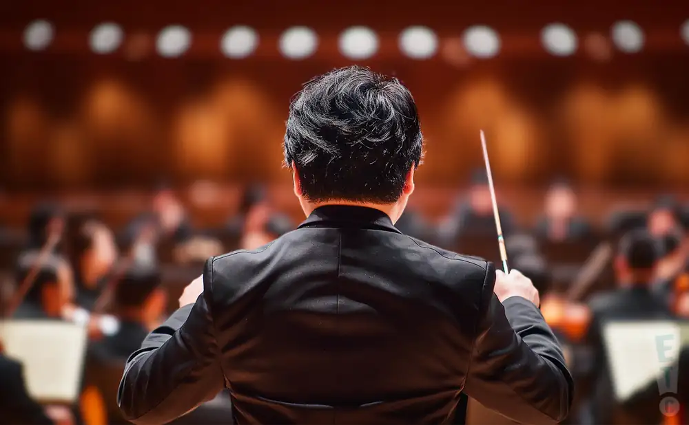 a rear view photo of kahchun wong conducting a symphony on stage before an audience