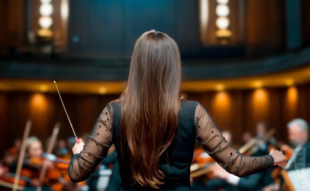 a rear view photo of marta gardolinksa conducting a symphony on stage before an audience