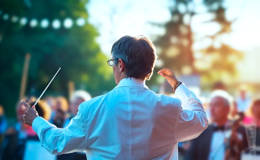 a photograph capturing american conductor peter bay as he leads an orchestra on an outdoor concert stage.