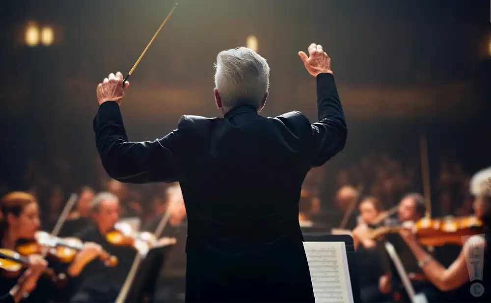 a rear view photo of peter oundjian conducting a symphony on stage before an audience