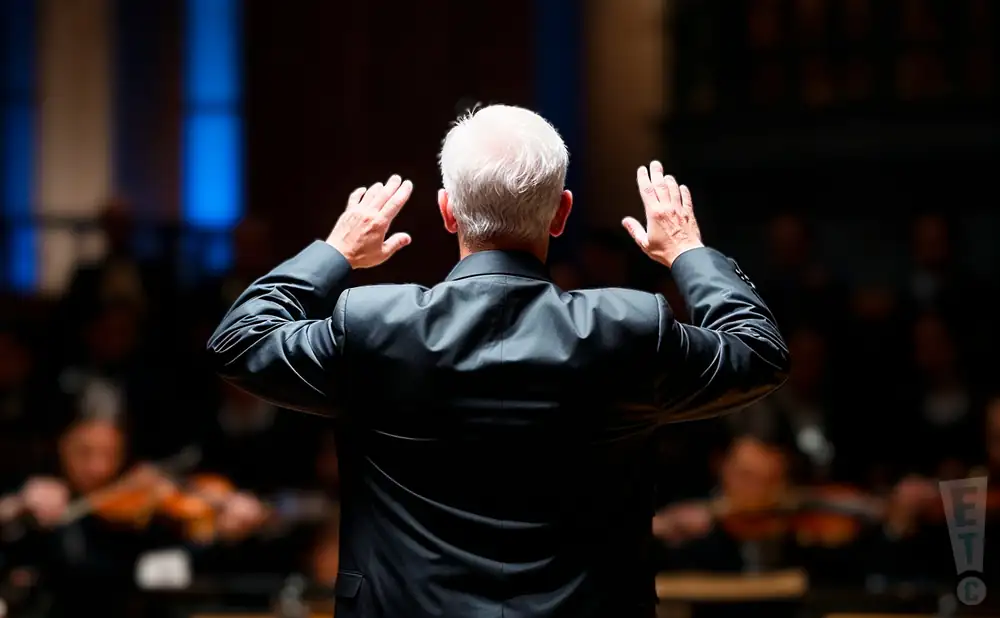a rear view photo of piotr gajewski conducting a symphony on stage before an audience