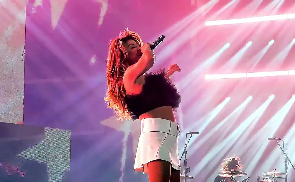 shania twain performing on stage in a black furry top and white skirt