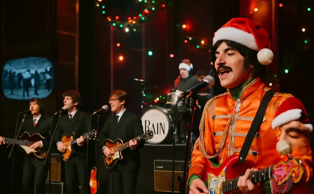 A band in Santa hats performs in front of Christmas lights. One guitarist wears an orange jacket.