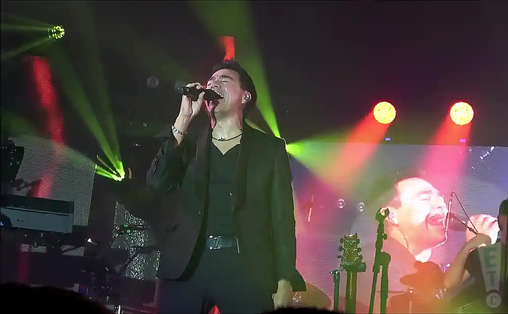 los temerarios singer singing under red and yellow lights with bass player in the background