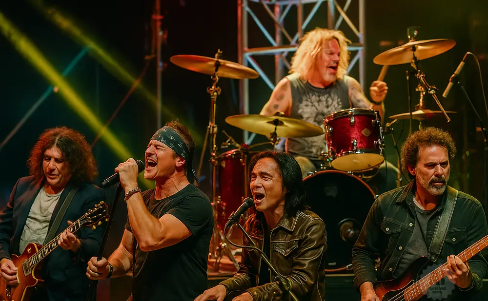 A rock band performs on stage with spotlights, the singer is in the foreground singing into a microphone.