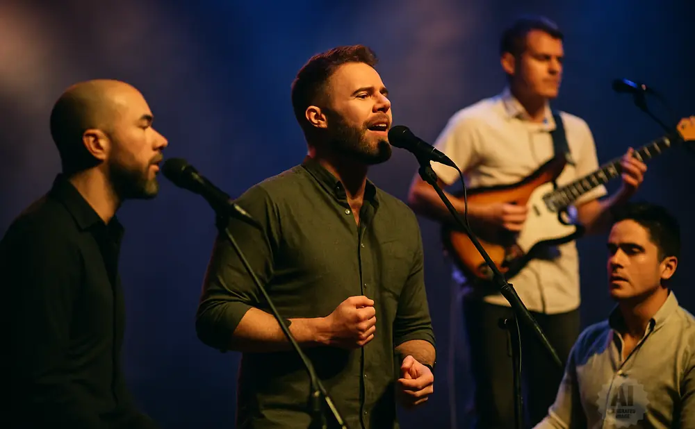 A band of four men perform on stage, with two singers at microphones, one guitarist, and one pianist.
