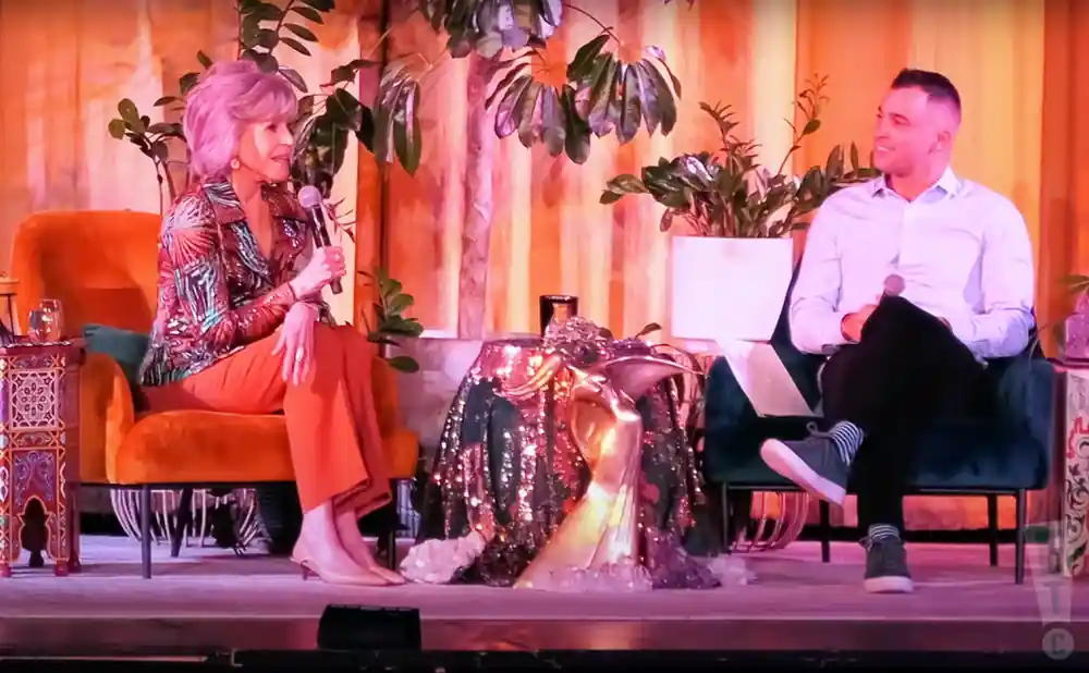 jane fonda sitting on stage talking to a man.