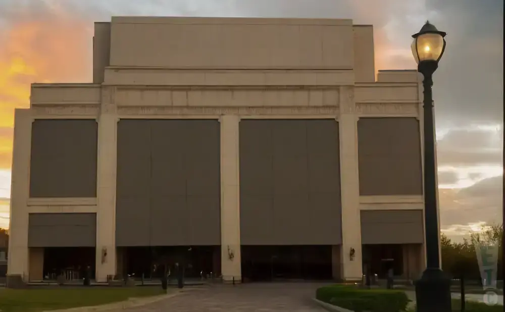 A large, beige building with large, covered windows is lit by a lamppost at sunset.