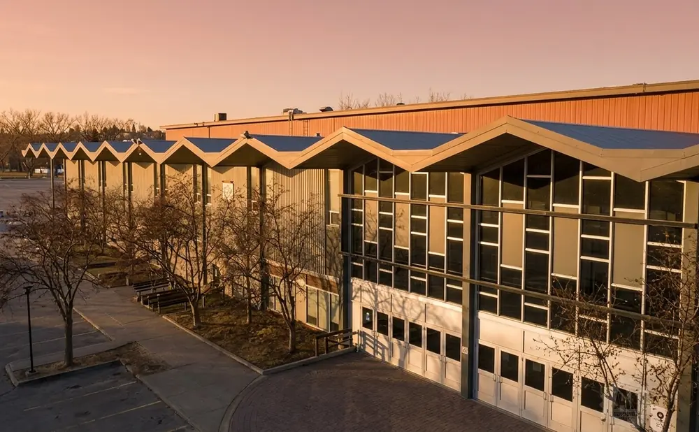Modern building with zigzag roof and large windows, at sunset.