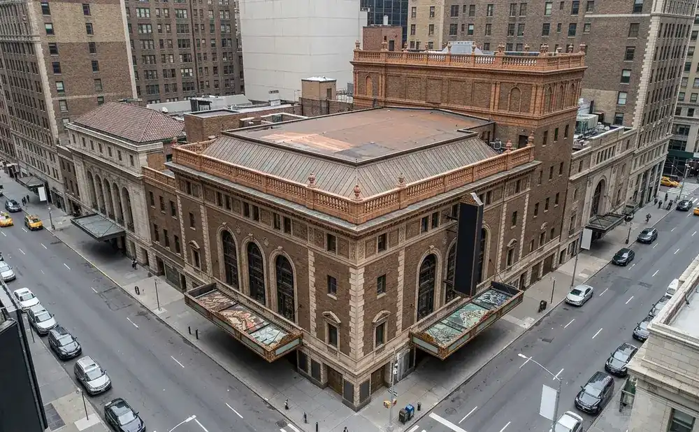 An aerial view of a tan brick building on a city street with cars and yellow taxis.