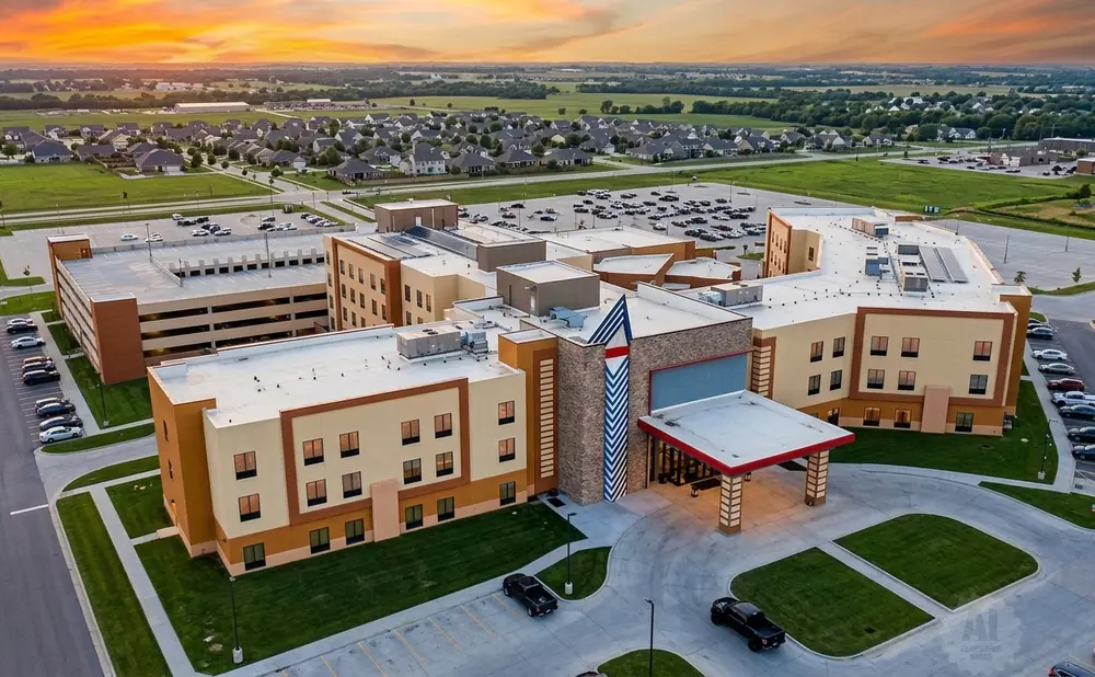 Aerial view of a modern hotel with a parking garage and surrounding suburban landscape at sunset.