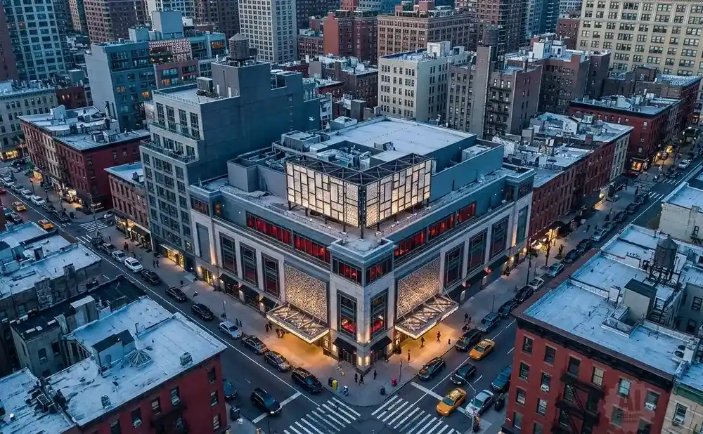 Aerial view of a city intersection with a large building featuring a unique glass and metal structure on top.