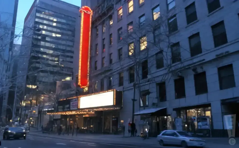 A vintage theater marque glows with lights on a city street at dusk.