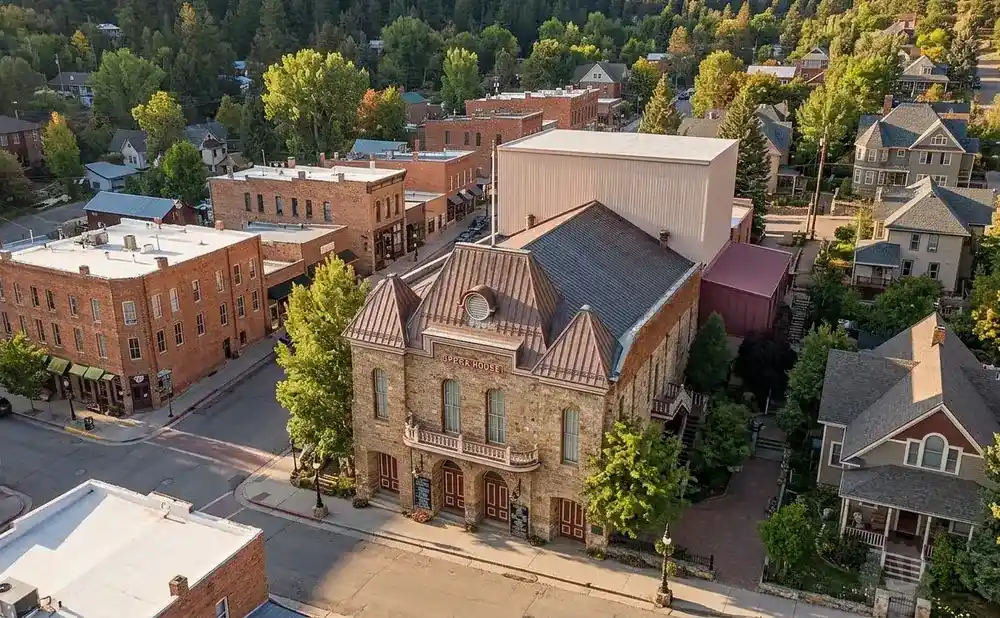 Aerial view of a historic opera house and surrounding buildings in a town nestled among trees.