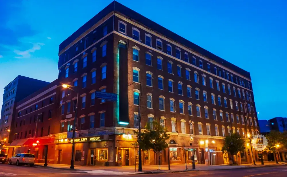 Evening shot of a brick building with many windows illuminated by warm light.