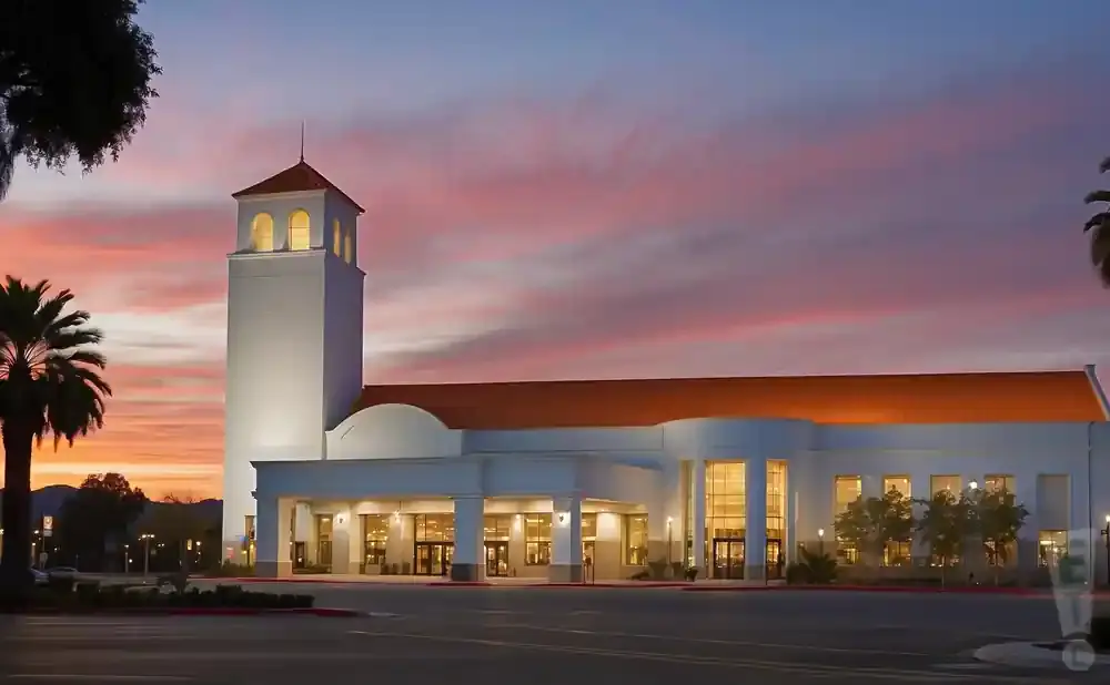 A white building with a tower and orange roof at sunset.