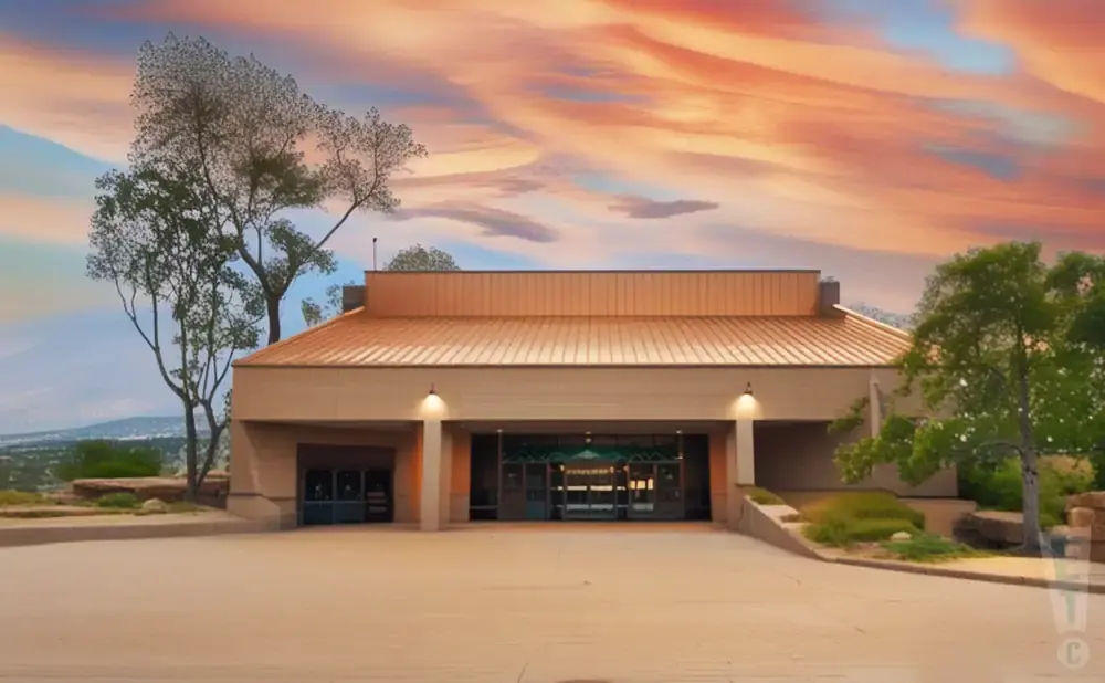 Modern building with a copper roof at sunset, surrounded by trees and desert landscape.
