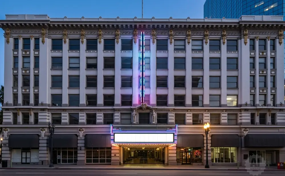 Exterior of a historic theater with neon lights and a marquee at dusk.