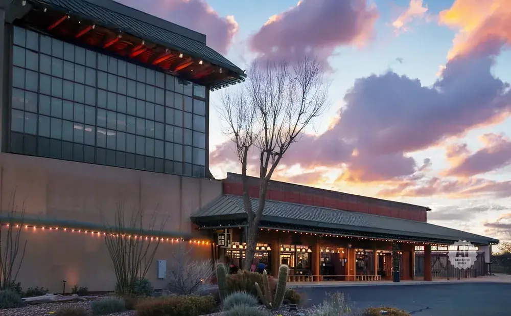 A modern building with large windows and red accents, set against a sunset sky with purple and orange clouds.