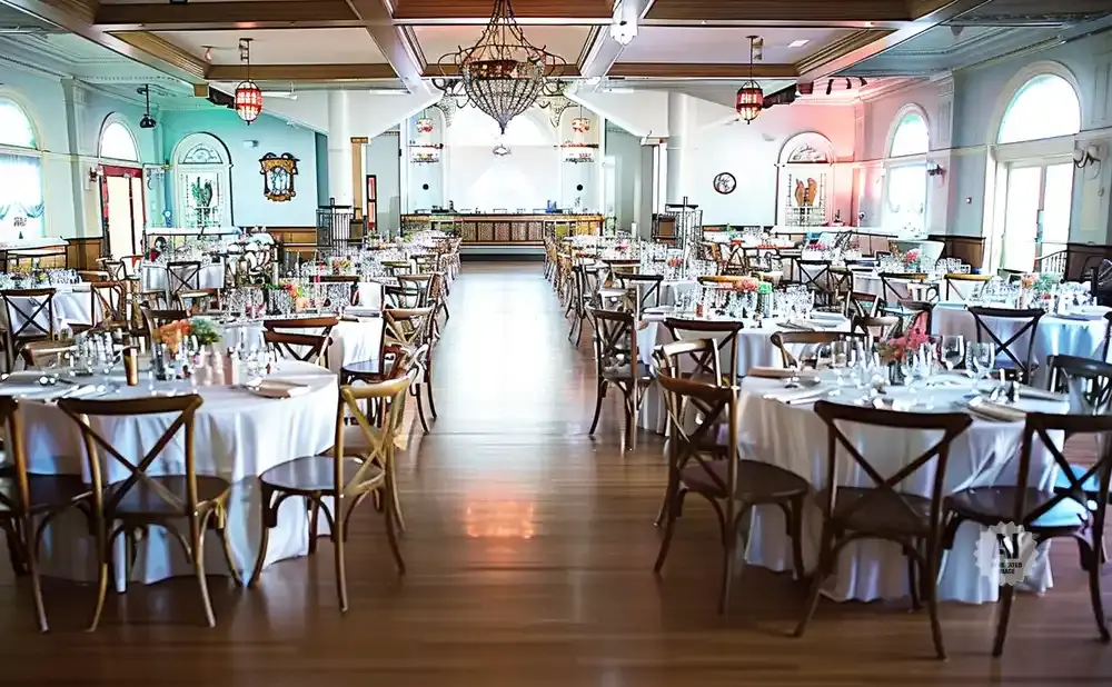 A beautifully decorated banquet hall set for a wedding reception with round tables, white tablecloths, and elegant wooden chairs.