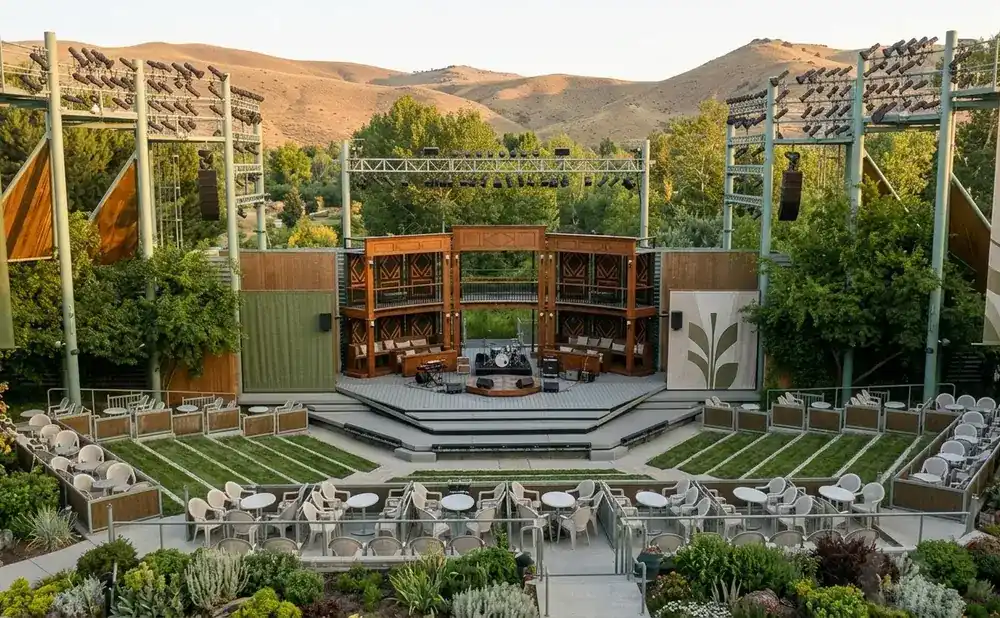 An outdoor amphitheater stage with seating, set against a backdrop of hills and trees.