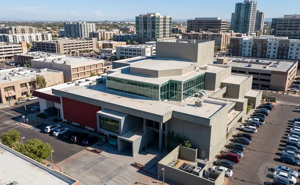 Aerial view of a modern, multi-story building with a large glass atrium and surrounding parking lots filled with cars.