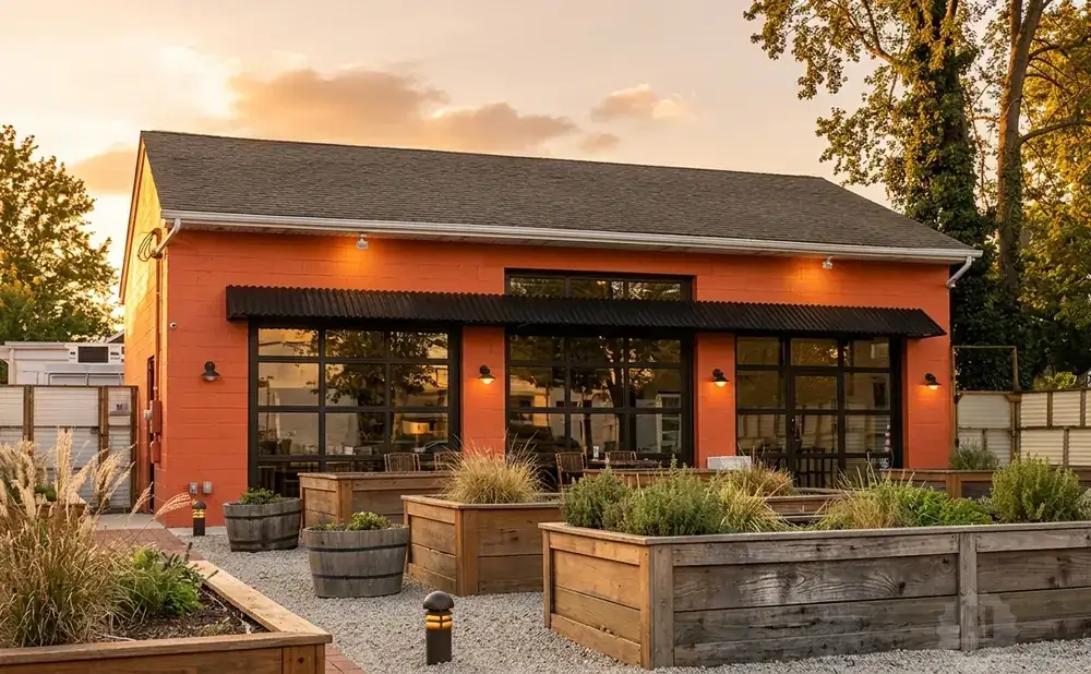 An orange building with large windows and an outdoor seating area with planters.