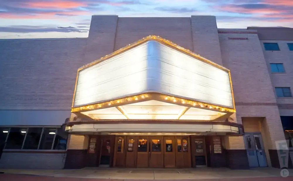 A brightly lit marquee theater at dusk with a colorful sky.