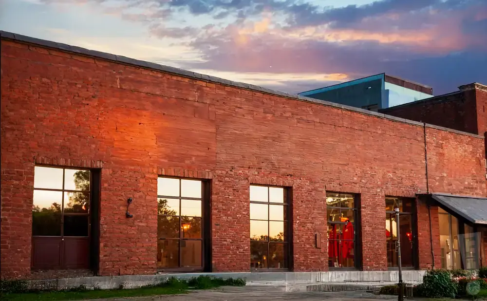 Exterior of a red brick building with large windows reflecting a sunset sky.