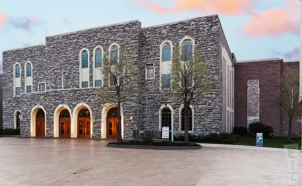 Exterior view of a stone building with arched doorways and windows, and trees in front.