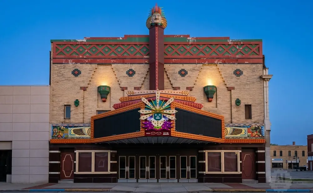 Art deco theater with elaborate facade featuring a Native American head, colorful sunburst, and marquee.