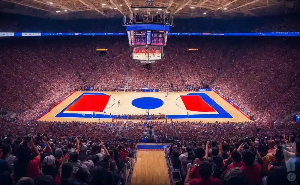 Basketball game in a packed arena with red and blue court markings and a large scoreboard.