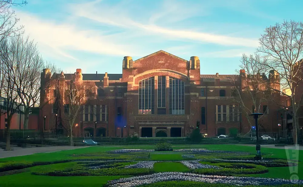 Large brick building with a grand arched window and a manicured garden in front.