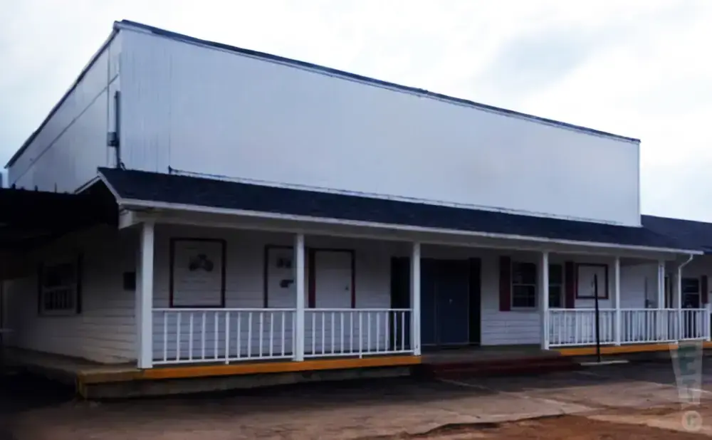 A white building with a long porch and a large blank sign above.