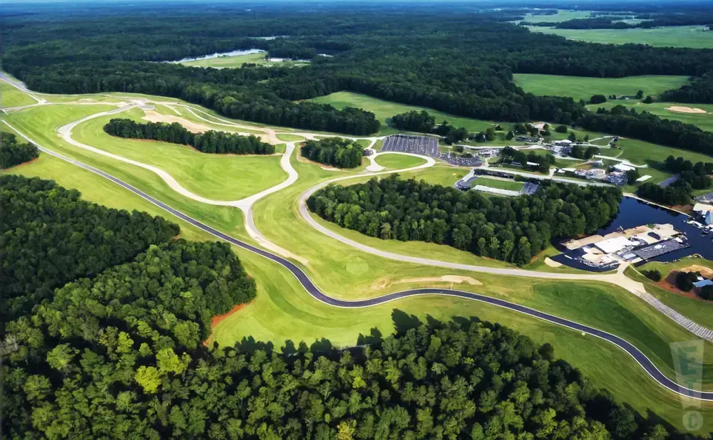 Aerial view of a winding race track surrounded by lush green forests and fields.